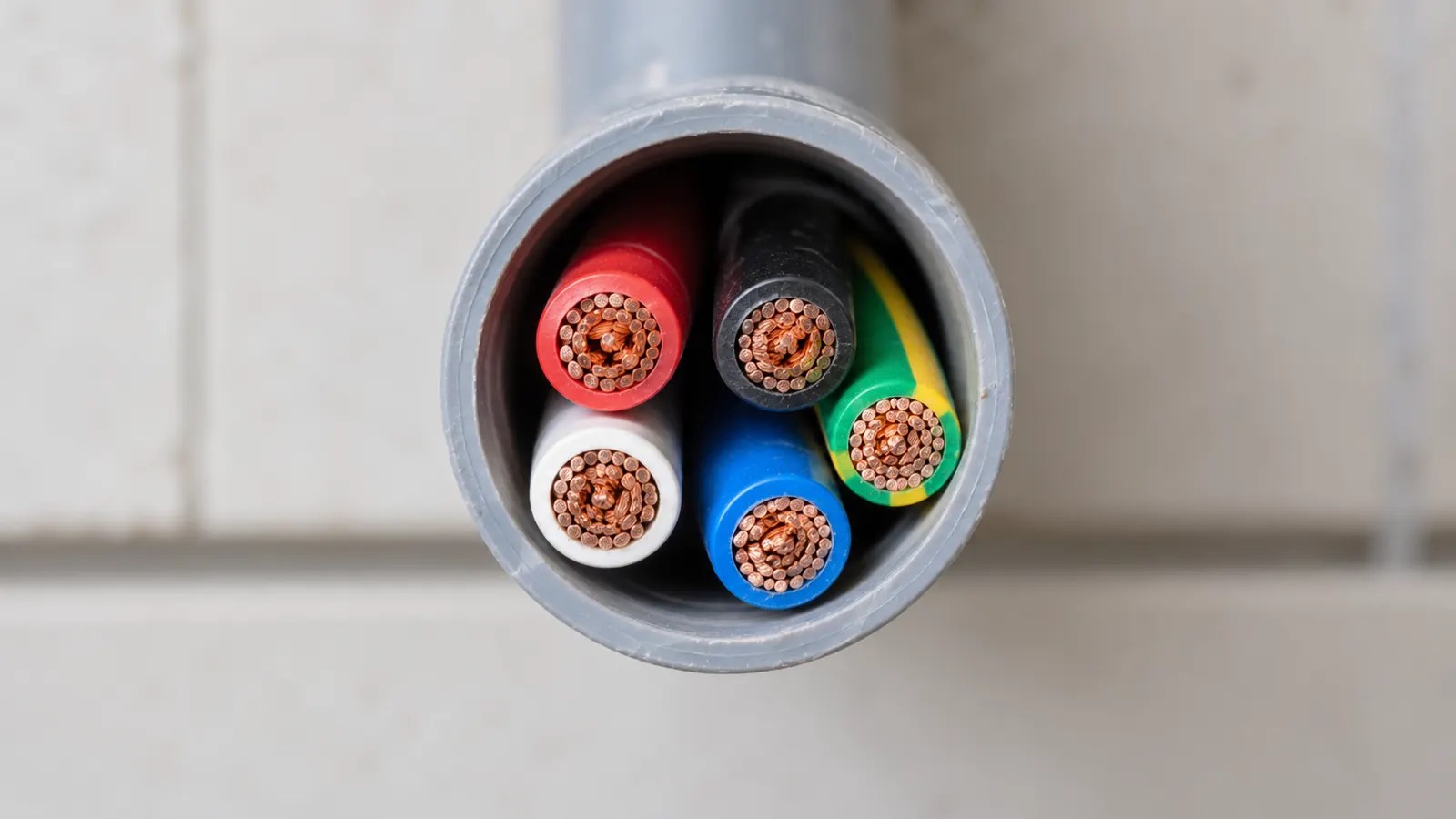 The open end of a grey conduit packed with several insulated cables.